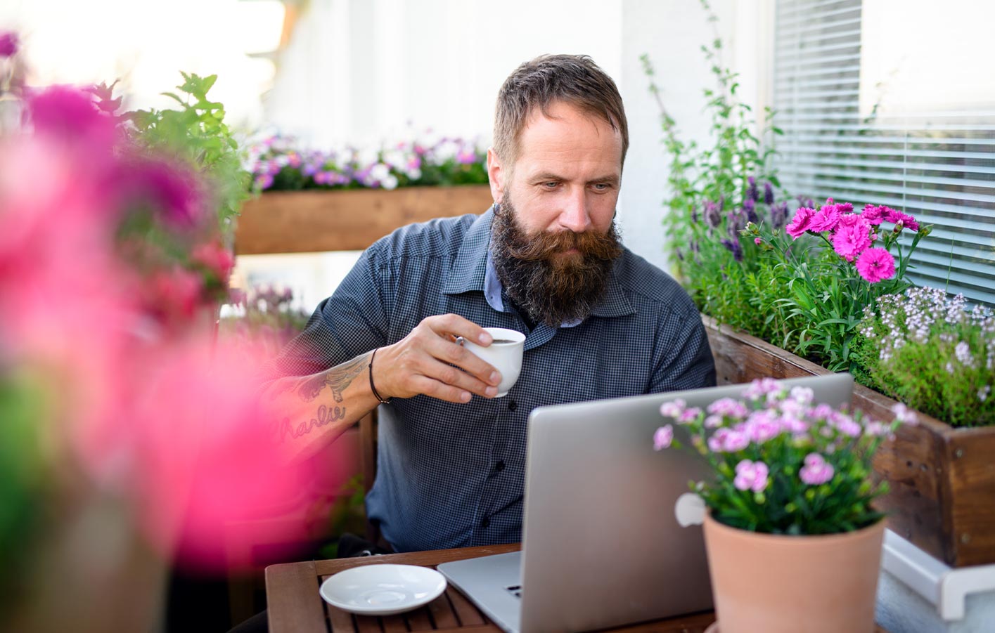 Mann arbeitet entspannt mit Kaffee am Laptop auf seiner Terrasse  