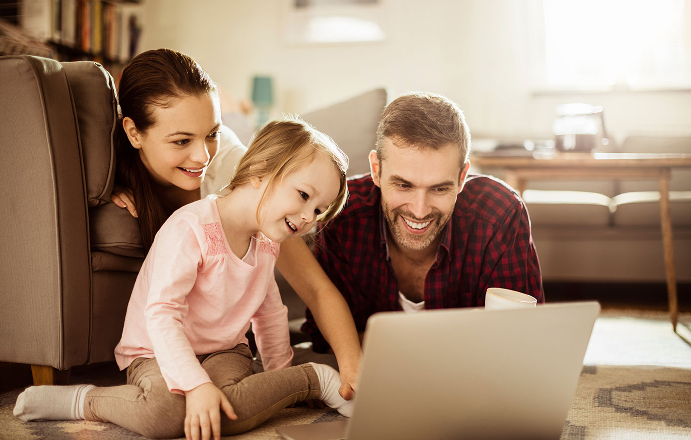 Familie sitzt auf dem Boden und schaut gemeinsam auf ein Notebook.